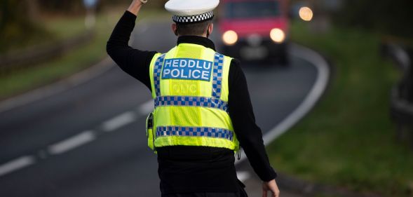 A Dyfed-Powys police officer stands by a nearby road.