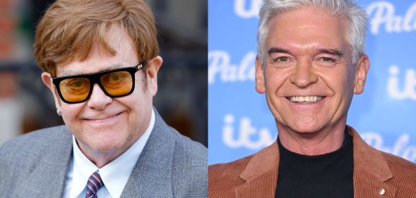 On the left, Elton John in black and yellow glasses, a grey suit, white shirt and blue and purple tie. On the right, Phillip Schofield in a black t-shirt and brown jacket. Both are smiling at the camera.