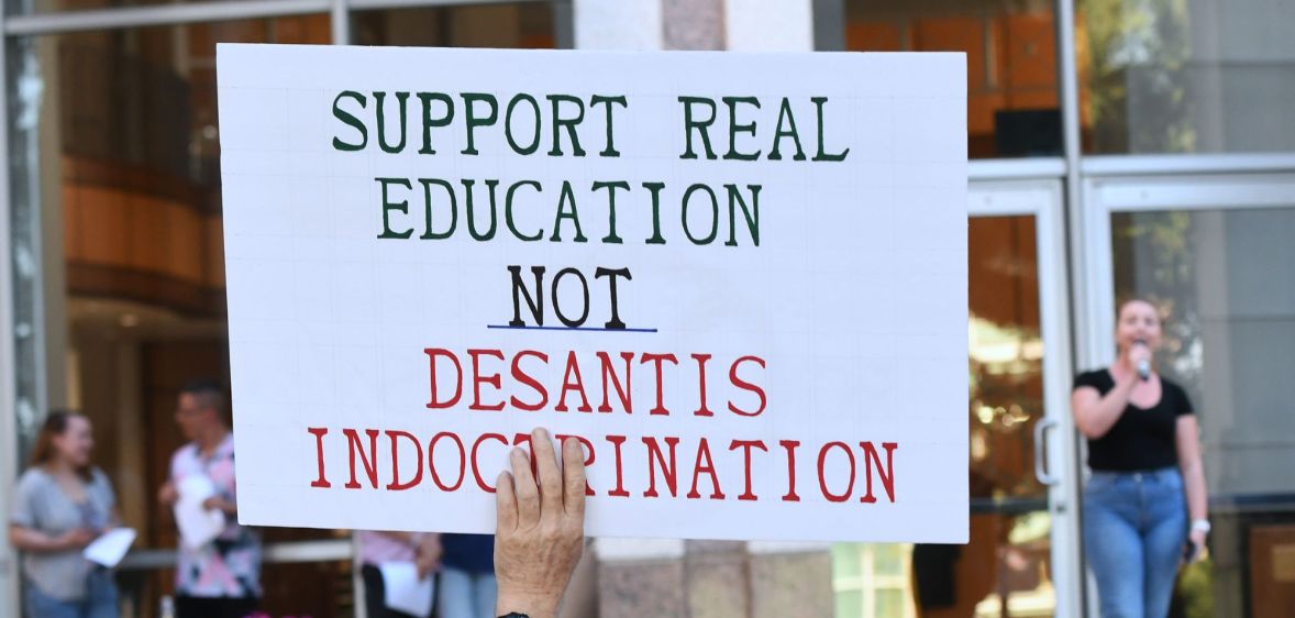 During a Florida protest, a protestor holds up a sign reading "Support real education, not DeSantis indoctrination."