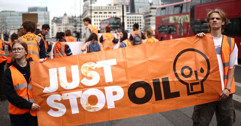 Two Just Stop Oil protesters hold a large orange banner with the organisation's name