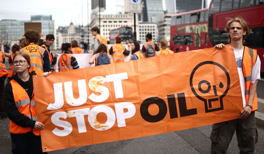 Two Just Stop Oil protesters hold a large orange banner with the organisation's name