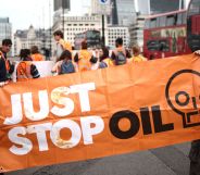Two Just Stop Oil protesters hold a large orange banner with the organisation's name