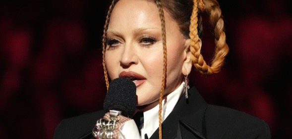 Madonna wears a suit and multiple rings, and she holds a microphone