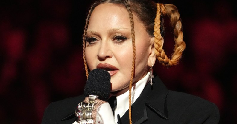 Madonna wears a suit and multiple rings, and she holds a microphone