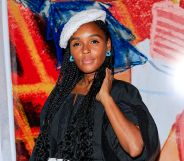 US singer and actor Janelle Monáe wears a black top, white beret and blue earring while standing against a red, orange, white and blue background.