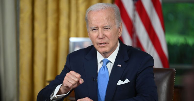 US President Joe Biden sits at a desk with an American flag behind him, delivering a talk from the White House