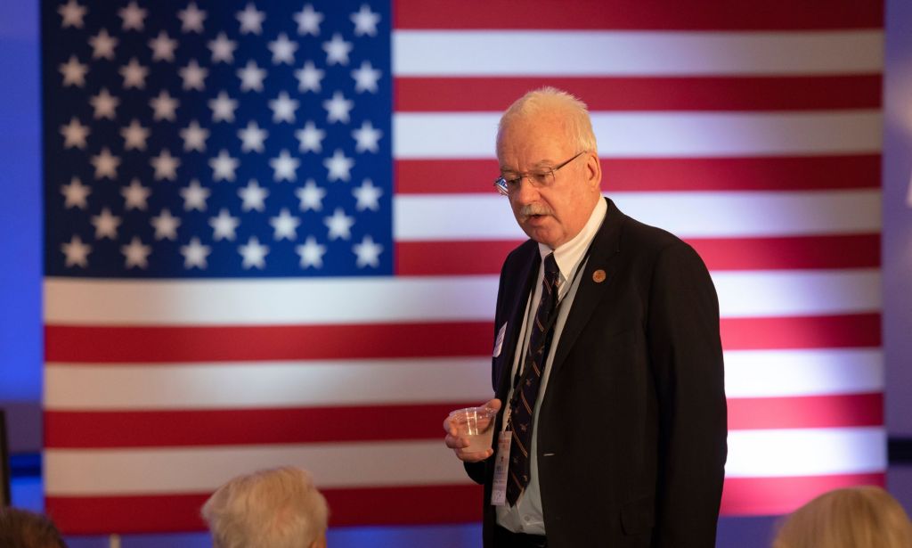 Arizona senator John kavanagh speaks to a member of the audience, standing infront of an American flag.