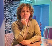 In this photo, Campaign Magazine's first transgender columnist Marty Davies is seen with curly brown hair and a khaki coloured shirt leaning on a table.