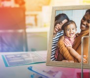 This is an image of an LGBTQ couple with their child in a picture frame. In the background is an office setup that is creatively overlayed with a prism.