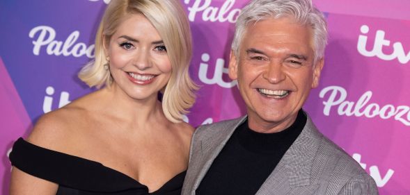 Holly Willoughby wears a black dress as she stands alongside Phillip Schofield in front of a purple background