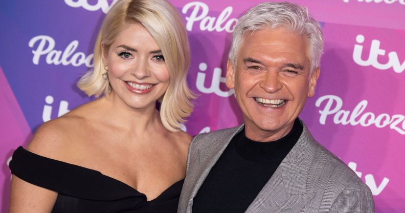 Holly Willoughby wears a black dress as she stands alongside Phillip Schofield in front of a purple background