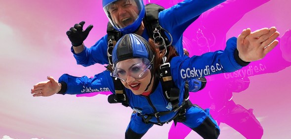 The image shows Rosie Zinfandel, a drag queen, skydiving. She is falling through the air and can be seen wearing full make-up and fake eyelashes.