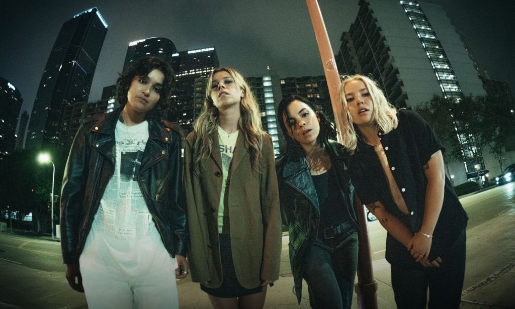 The Aces stand on a road in front of tall buildings as part of the promotional images for their third studio album I've Loved You For So Long. 