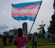 A person holding a trans flag in the sky.