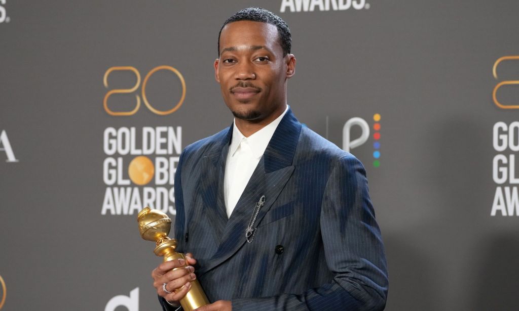 Tyler James Williams in a navy suit at the Golden Globes, holding his golden globe.