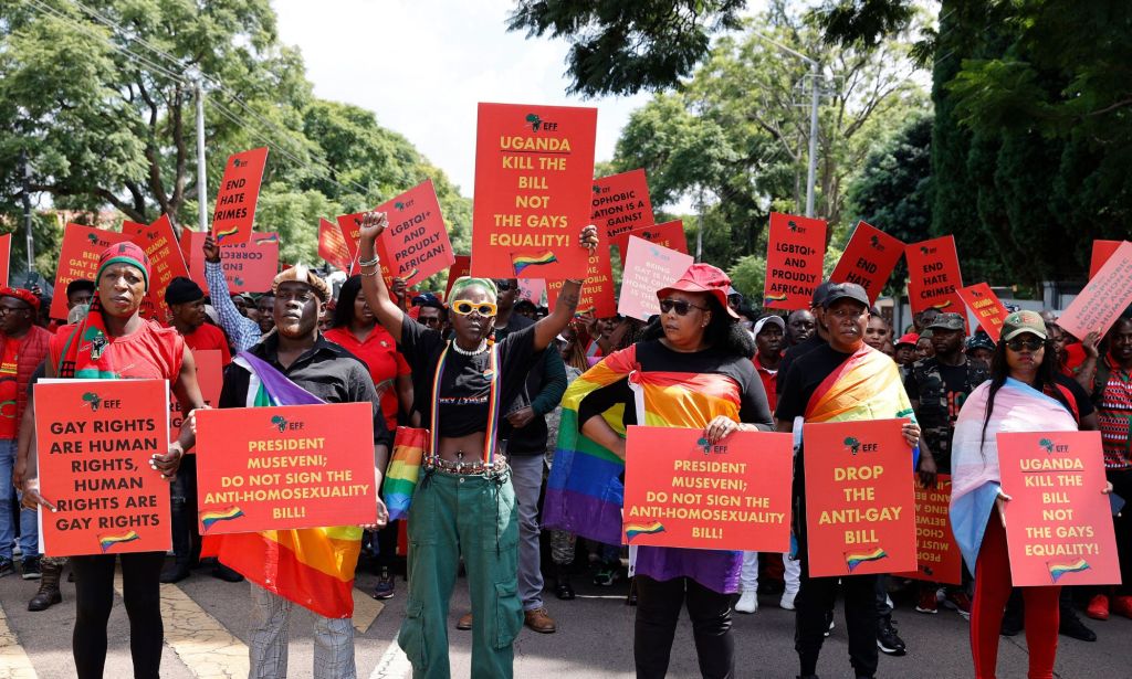 A group of LGBTQ+ Ugandans protest with red signs reading slogans of equality.