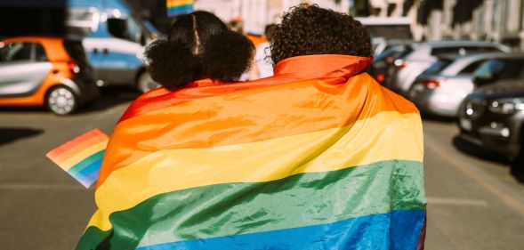 Two people facing backwards wrapped in a Pride flag