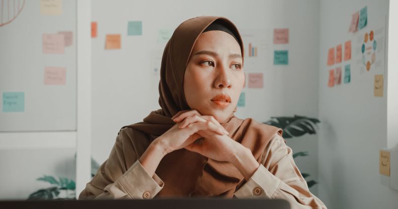 Woman wearing a brown hijab folds her hands under her chin