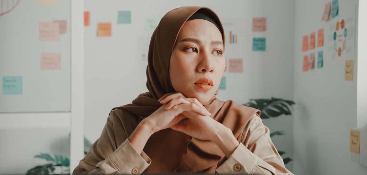 Woman wearing a brown hijab folds her hands under her chin