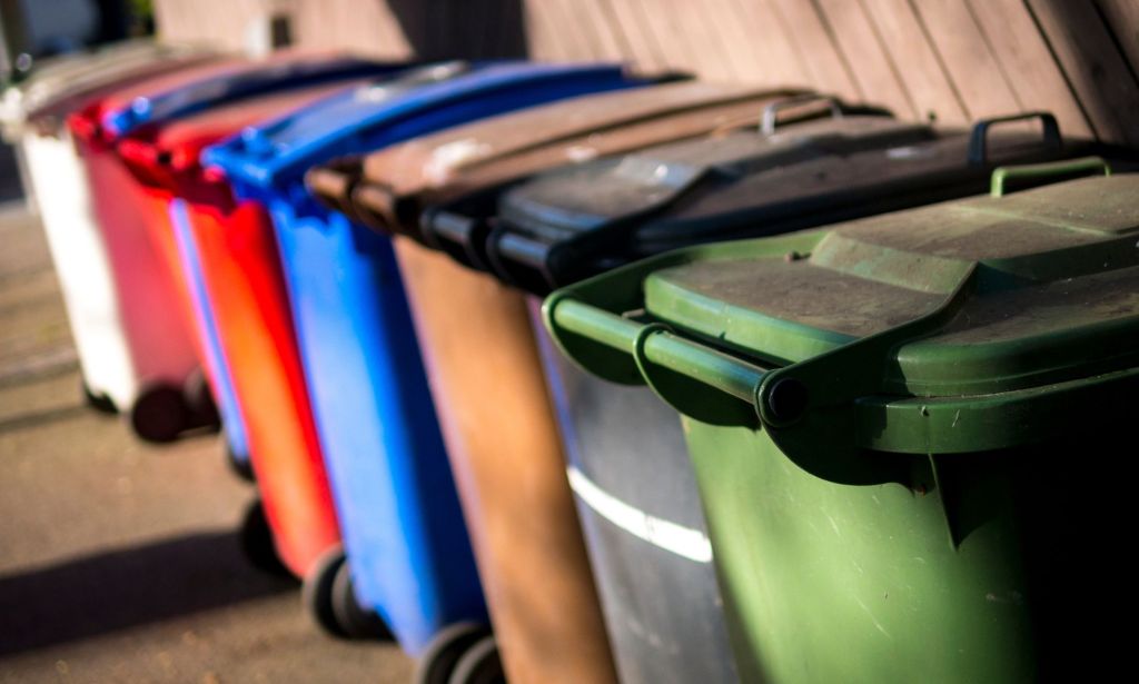 A set of UK wheelie bins, each a different colour, lined up against one another.
