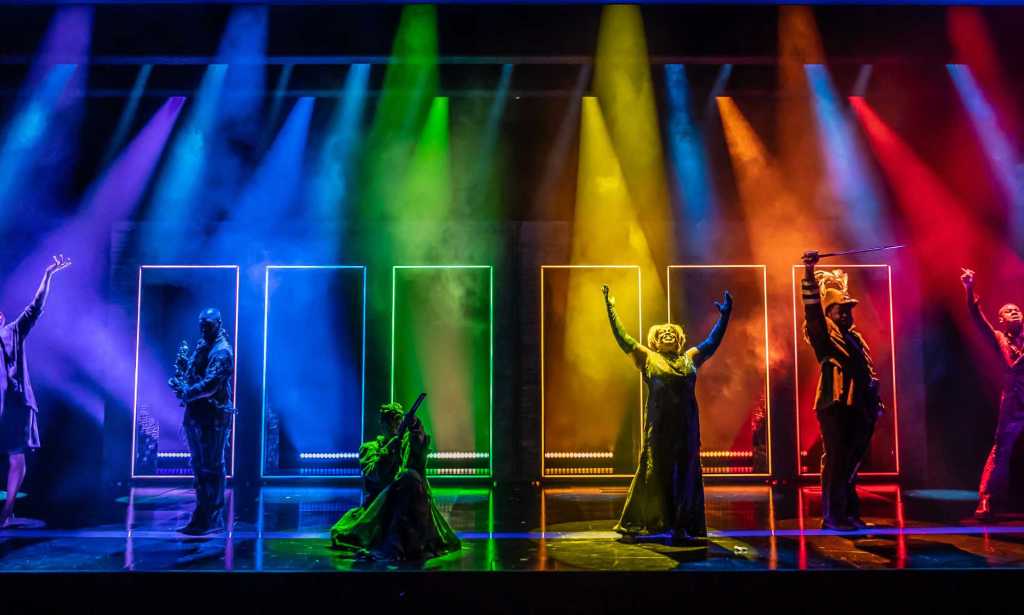 Seven figures on stage with lights shining a rainbow over them