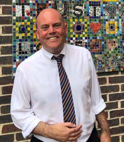 Andrew Moffat delivers LGBTQ+ inclusive education. He is pictured here wearing a white shirt and a tie.