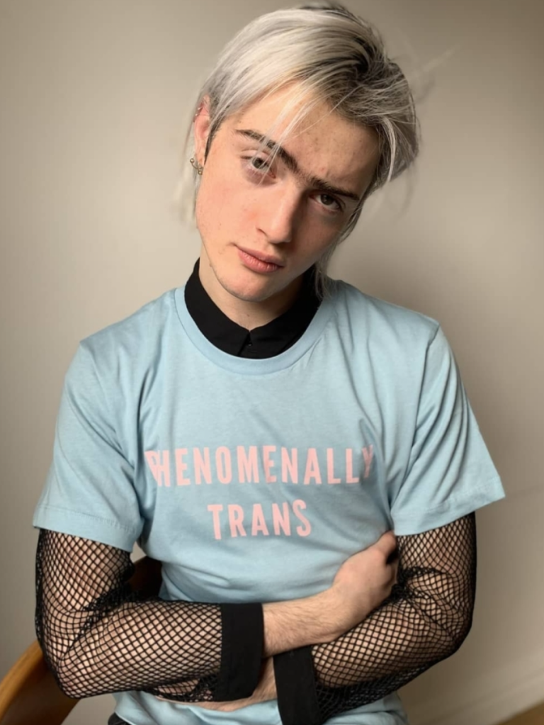 Model Casil McArthur wears a light blue shirt with pink letters reading 'phenomenally trans' over black a black fishnet top