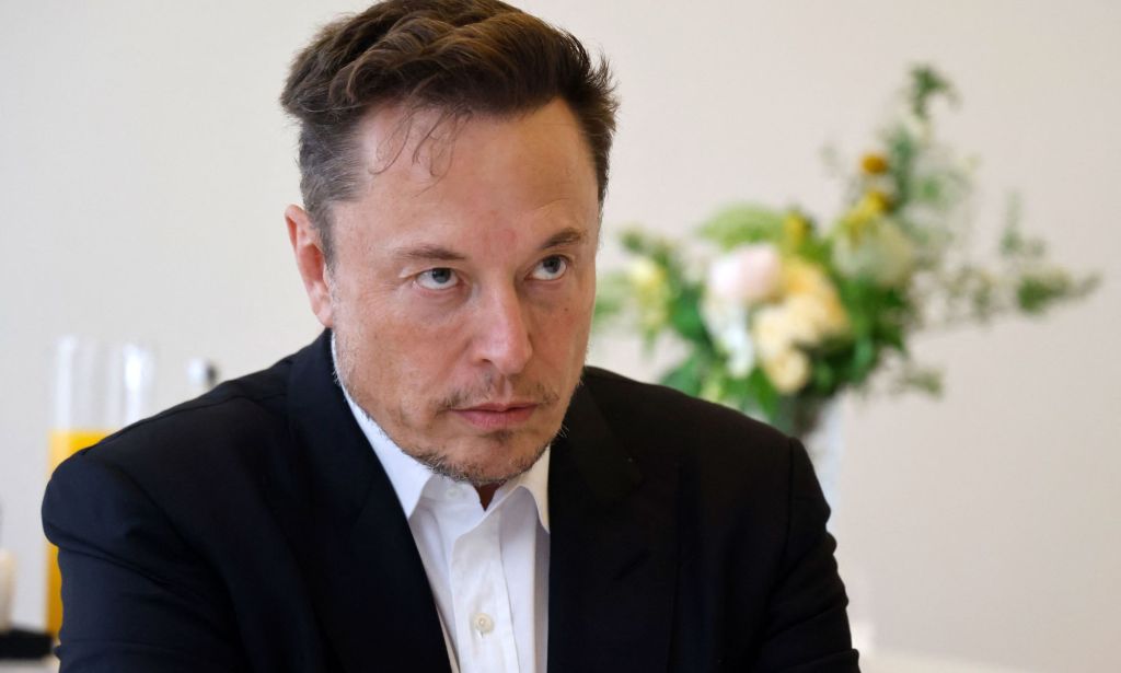 Twitter boss Elon Musk wears a white shirt and black coat as he stares at someone off camera