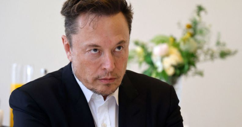 Twitter boss Elon Musk wears a white shirt and black coat as he stares at someone off camera