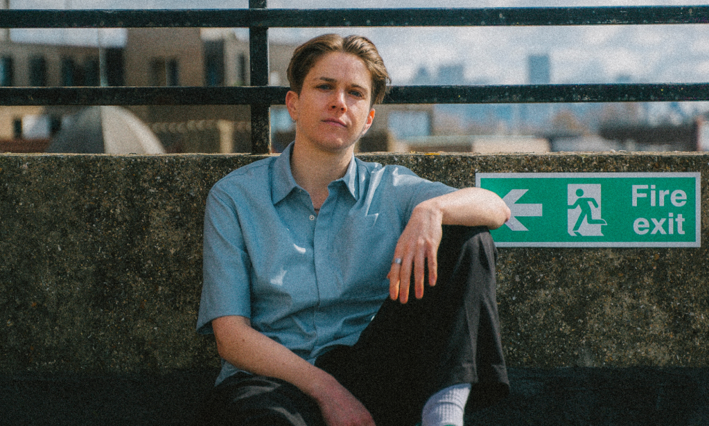 Heff sits against a railing wearing a blue shirt and chinos