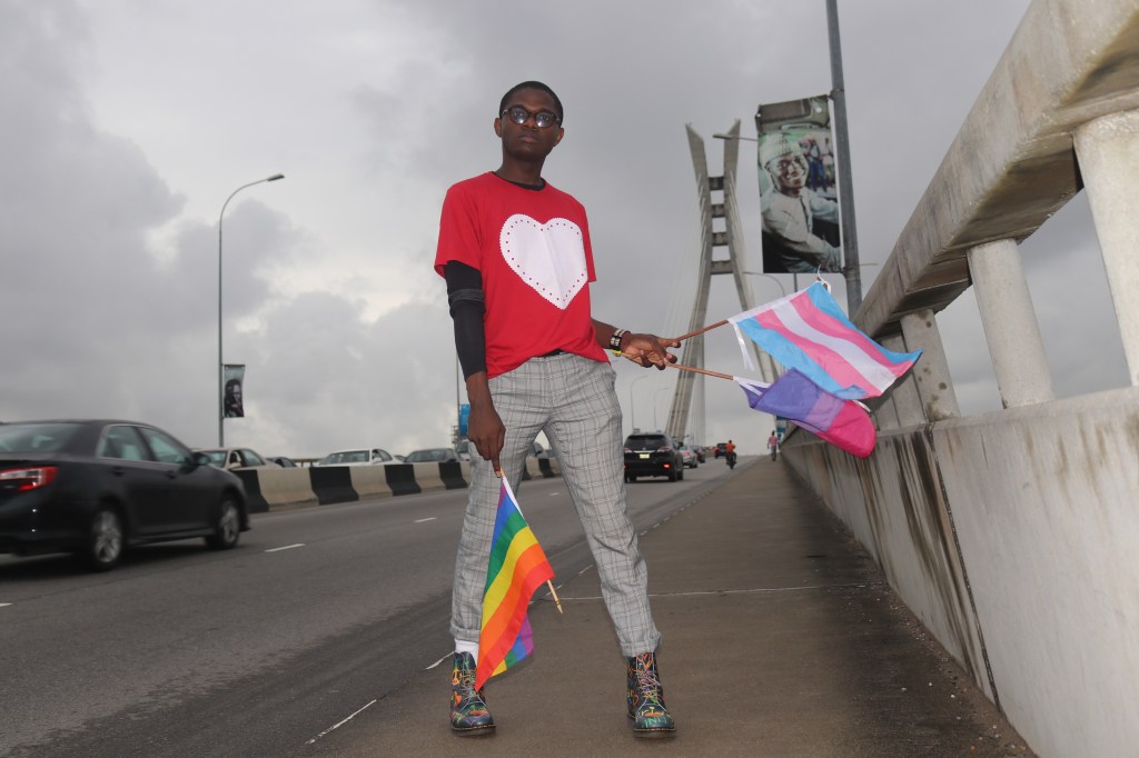 Joel is pictured here holding Pride and trans flags by the side of a road.