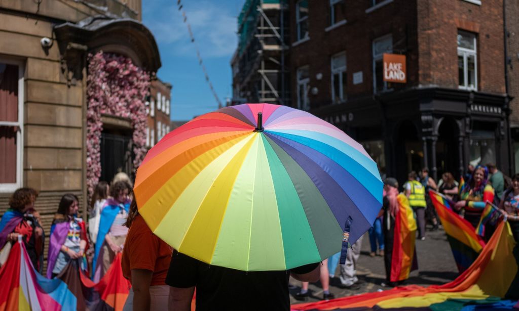 A person holds up a rainbow umbrella during a LGBTQ+ Pride Month celebration in the UK as they walk down a busy street
