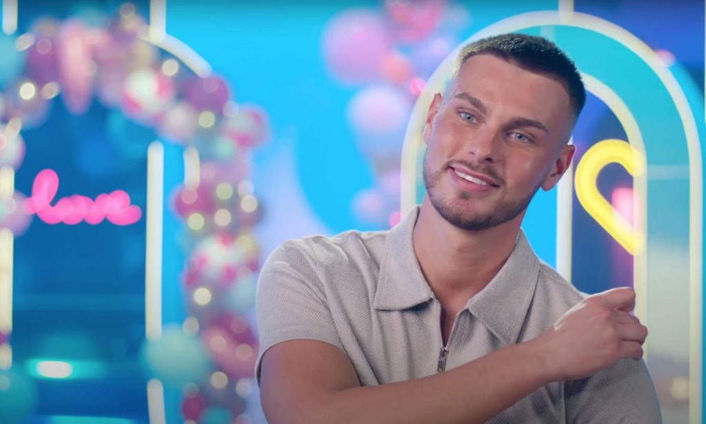 Love Island 2023 contestant George Fensom wears a grey shirt as he sits down for an interview