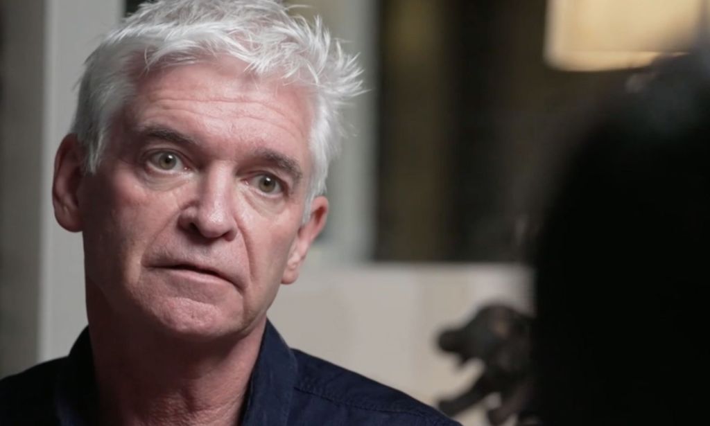 Phillip Schofield wears a dark shirt as he speaks to a BBC presenter who is off camera