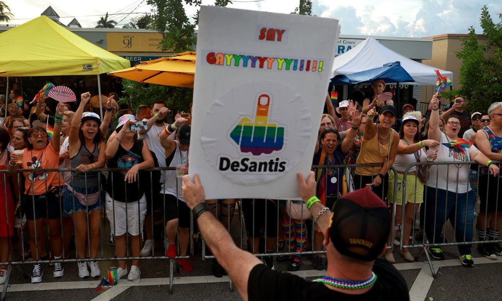 A person holds up a sign, written in rainbow lettering, that says 'Say gayyyyyyyyyy!!!!' with a middle finger and then the surname of Republican presidential candidate Ron DeSantis at an LGBTQ+ Pride event