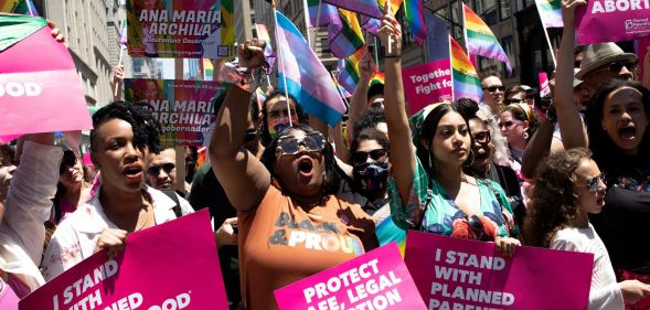 A crowd of people hold up signs in favour of reproductive rights and denouncing the Supreme Court for overturning Roe v Wade while holding LGBTQ+ and trans Pride flags