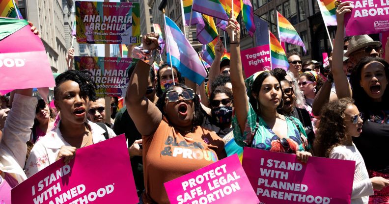 A crowd of people hold up signs in favour of reproductive rights and denouncing the Supreme Court for overturning Roe v Wade while holding LGBTQ+ and trans Pride flags