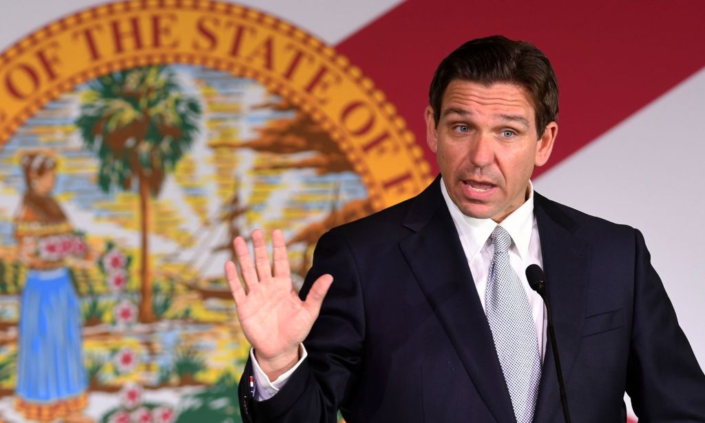 Republican presidential candidate Ron DeSantis holds up one hand as he speaks at a podium