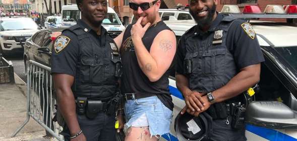 Sam Smith, a white non-binary person with blonde hair, posing in between two Black, male NYPD officers