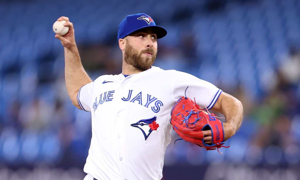 Toronto Blue Jays relief pitcher Anthony Bass wears a white uniform and blue baseball cap as he throws a baseball somewhere off screen