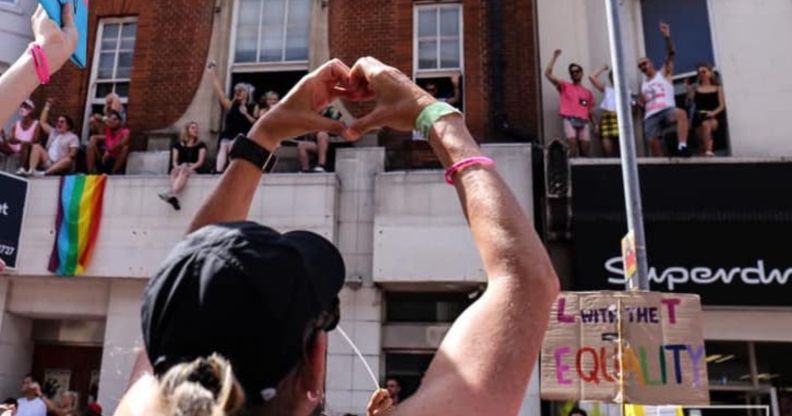 A person holds up their hands in the shape of a heart, to show their love, during an LGBTQ+ Pride event with a trans flag in the background