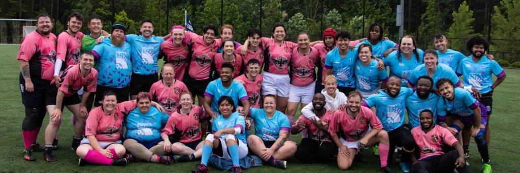 A group shot of multiple rugby players wearing pink and blue jerseys as they pose happily for the camera