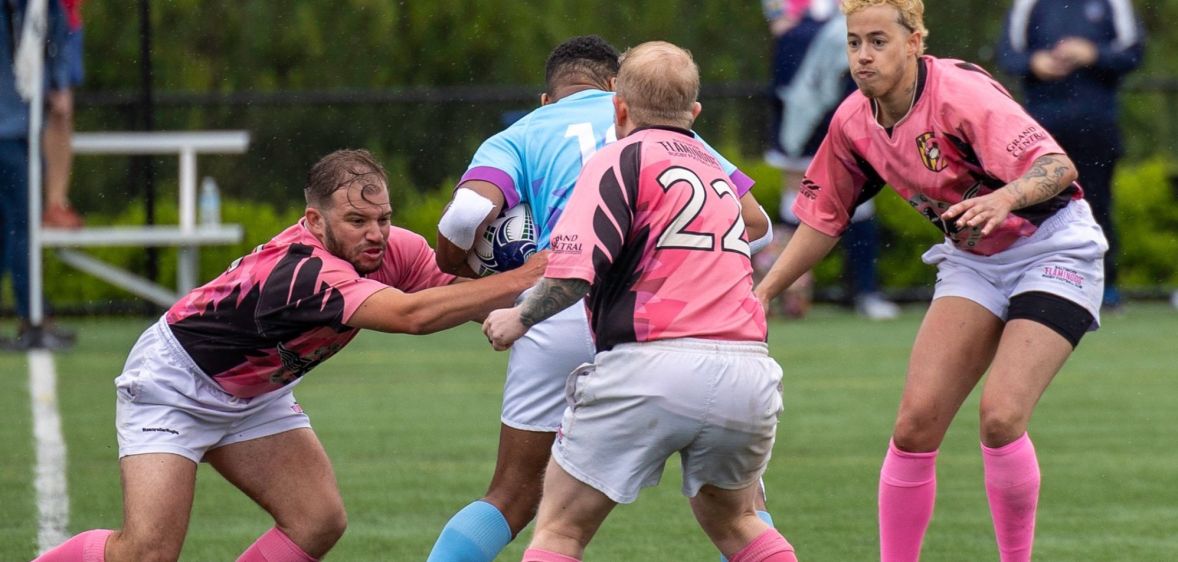 Trans rugby player Val Pizzo is mid tackle during an all-trans match in the US with various players wearing blue and pink jerseys