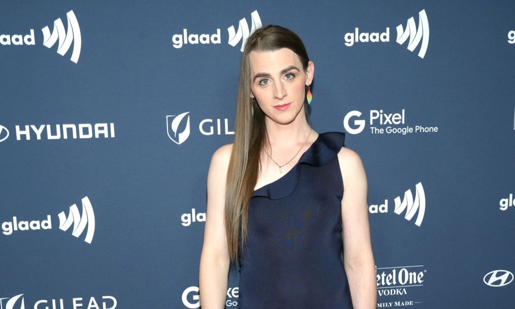 Trans lawmaker Zooey Zephyr wears a dark one shoulder dress and rainbow earrings as she poses for the camera