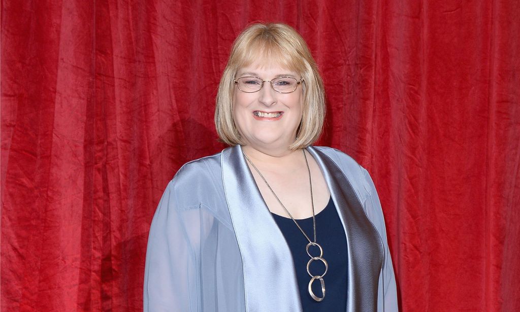 Annie Wallace in a blue jacket and navy top, wearing glasses and a silver necklace.