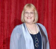 Annie Wallace in a blue jacket and navy top, wearing glasses and a silver necklace.