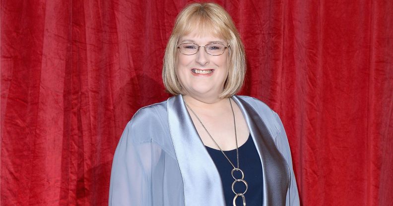 Annie Wallace in a blue jacket and navy top, wearing glasses and a silver necklace.