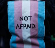 A person wears a jacket with a patch on the back of a trans flag that says "not afraid."