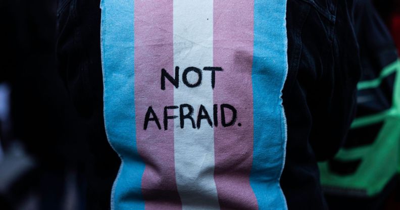 A person wears a jacket with a patch on the back of a trans flag that says "not afraid."
