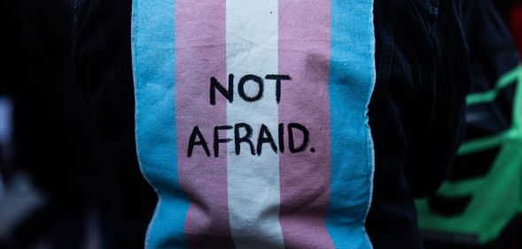 A person wears a jacket with a patch on the back of a trans flag that says "not afraid."